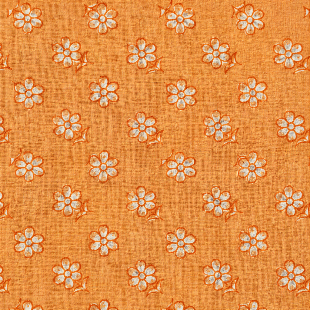 A close-up of orange fabric with a repeating pattern of small white flowers outlined in orange.